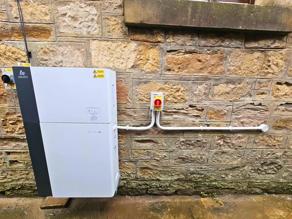 AlphaESS battery unit fitted on a traditional stone wall, cable run in white conduit to an isolator switch