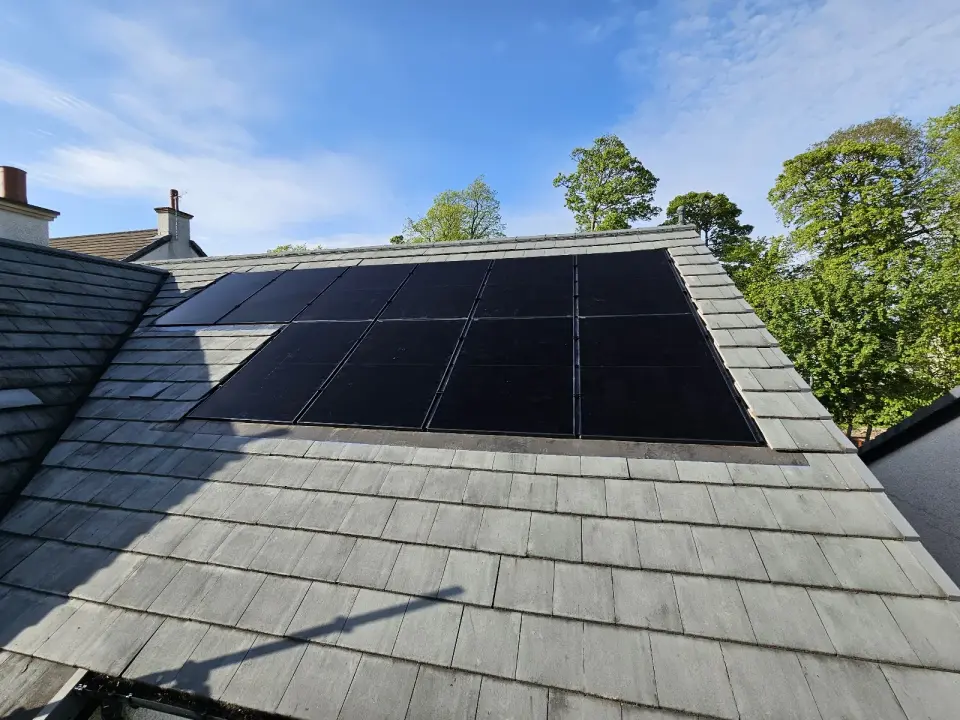 Solar panels fitted in a neat row on a slate roof, blue sky behind