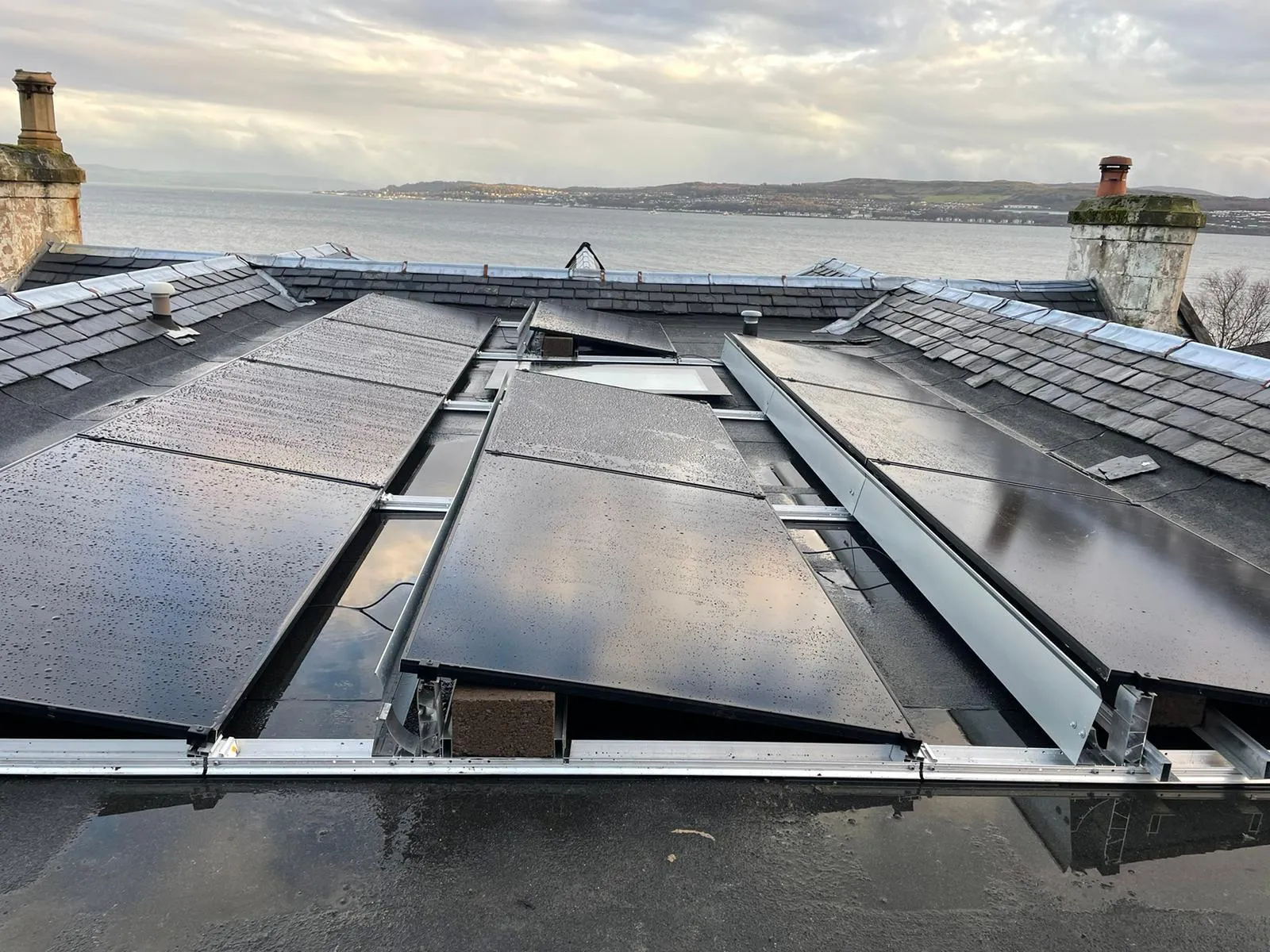 Panels on the low-pitched slate roof of a terraced property, chimney stacks and the water beyond