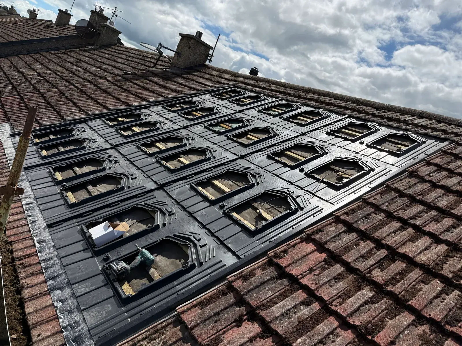 Installer fitting roof mounting trays partway through a solar panel installation.