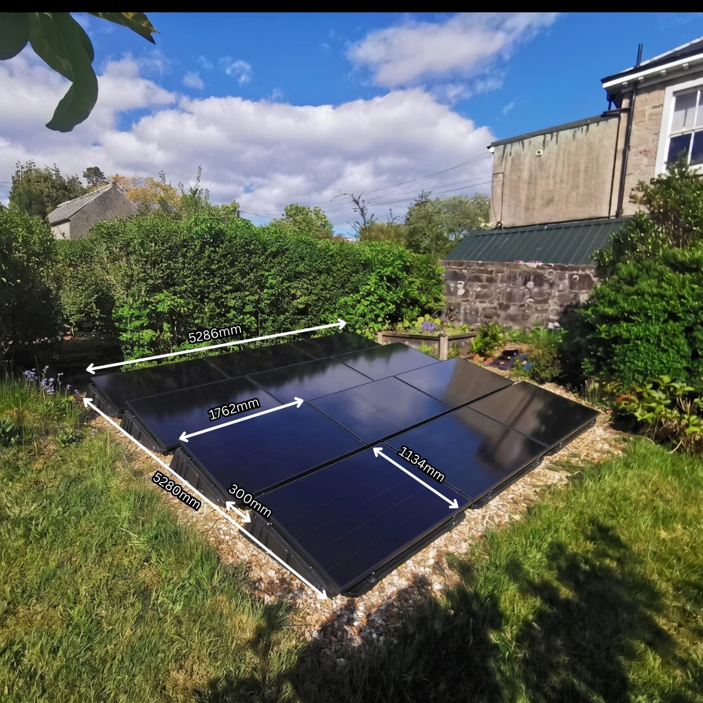A ground-mounted solar array on a garden bed, with its overall length, width and individual panel dimensions marked across the photo